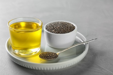 Plate with chia oil, seeds and spoon on grey background