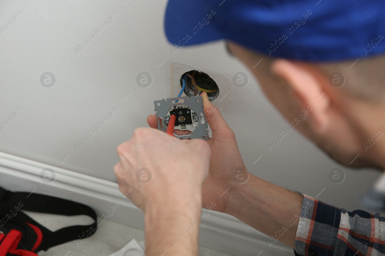 Photo of Electrician with screwdriver repairing power socket indoors, closeup