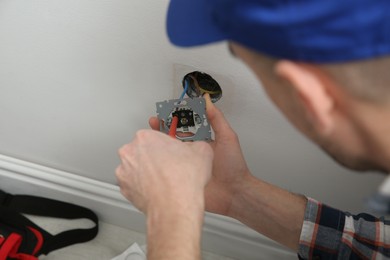 Photo of Electrician with screwdriver repairing power socket indoors, closeup