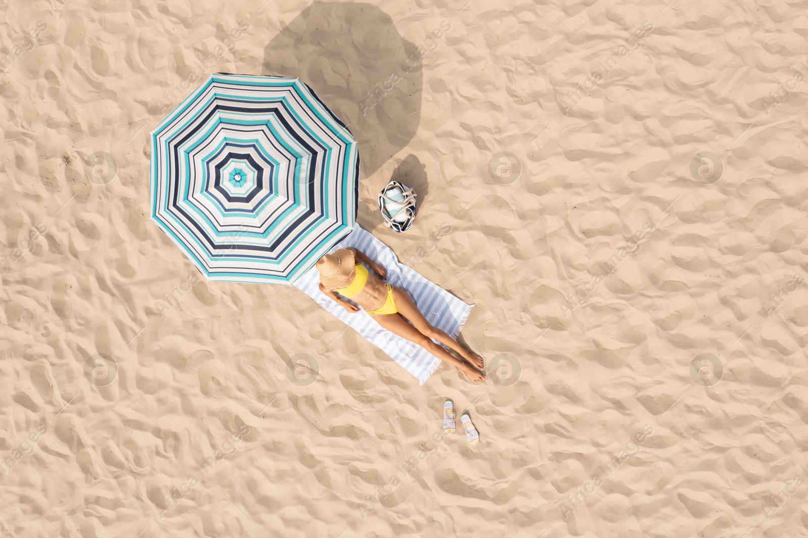 Image of Woman resting under striped beach umbrella at sandy coast, aerial view. Space for text