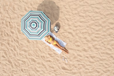 Woman resting under striped beach umbrella at sandy coast, aerial view. Space for text