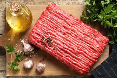 Raw ground meat, spices, parsley and oil on wooden table, top view