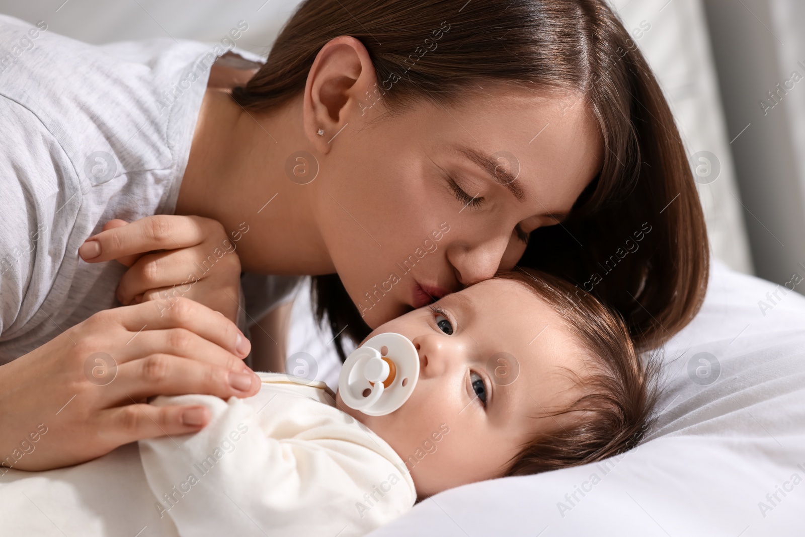 Photo of Happy mother kissing her little baby on bed