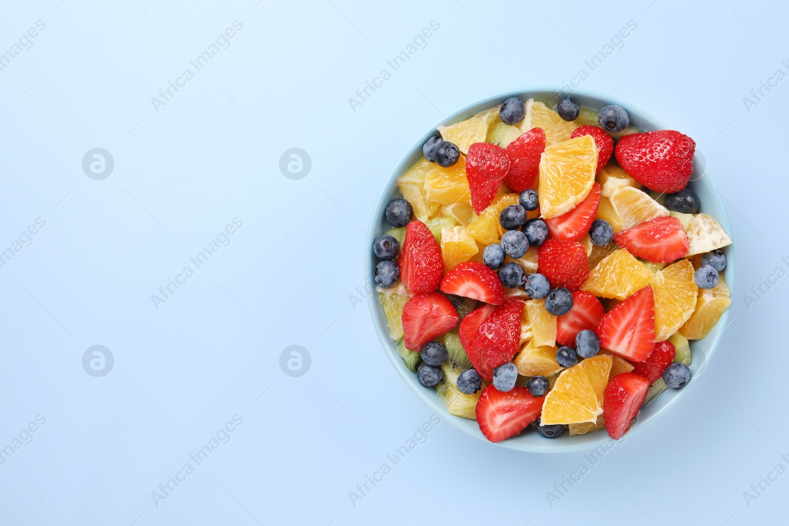 Photo of Yummy fruit salad in bowl on light blue background, top view. Space for text