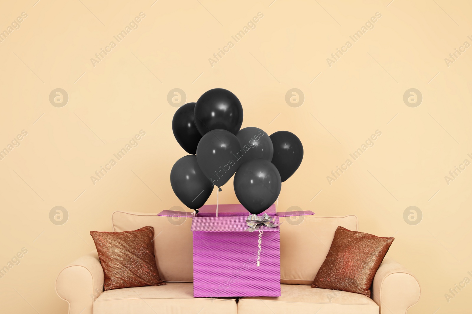 Image of Black Friday concept. Box with bunch of balloons on sofa near beige wall