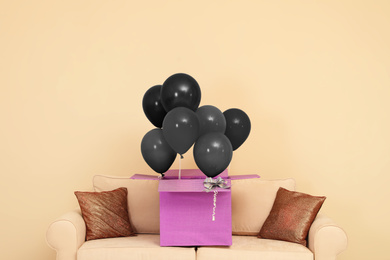 Black Friday concept. Box with bunch of balloons on sofa near beige wall