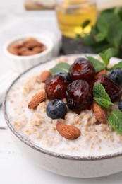 Photo of Tasty wheat porridge with milk, dates, blueberries and almonds in bowl on table, closeup