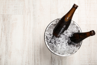 Photo of Beer in metal bucket with ice on white wooden table, top view. Space for text