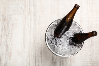 Beer in metal bucket with ice on white wooden table, top view. Space for text