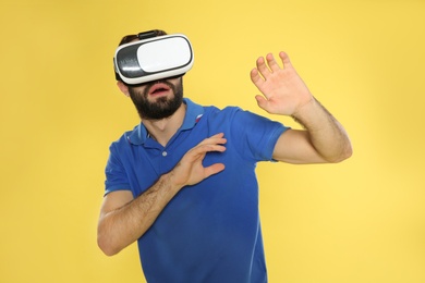 Emotional young man playing video games with virtual reality headset on color background