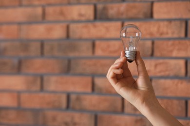 Photo of Woman holding light bulb near brick wall indoors, closeup. Space for text
