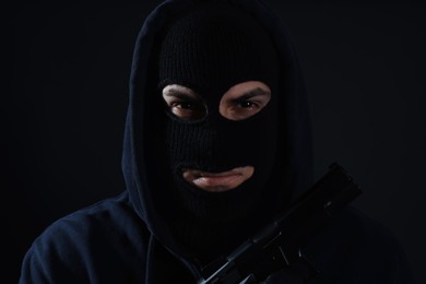 Photo of Man wearing knitted balaclava with gun on black background