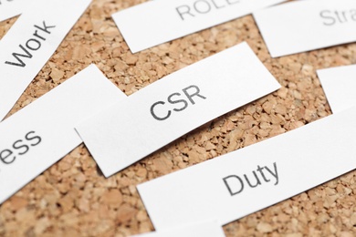 Photo of Paper sheet with letters CSR on corkboard, closeup. Corporate social responsibility concept