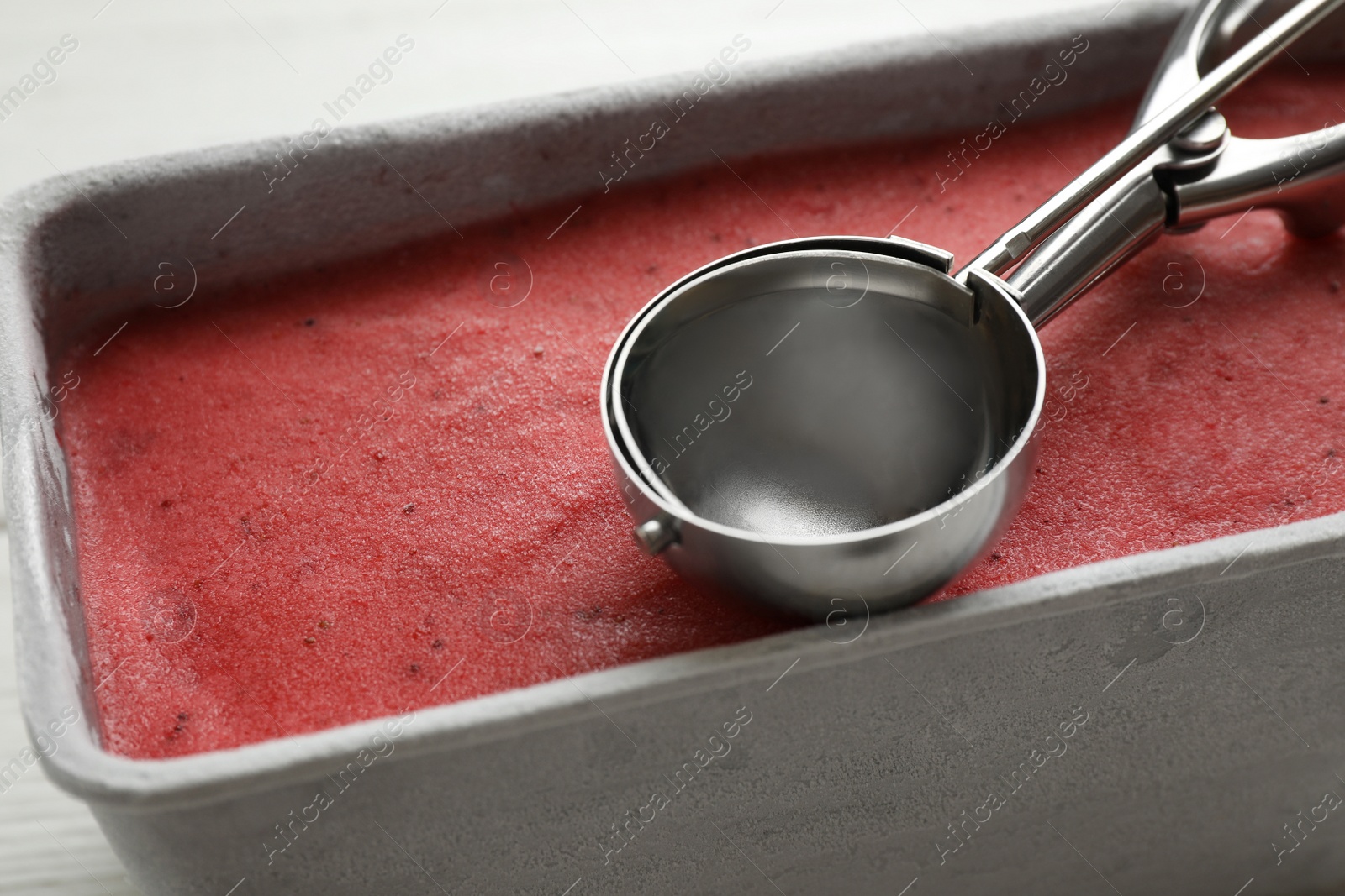 Photo of Container with delicious pink ice cream and scoop, closeup