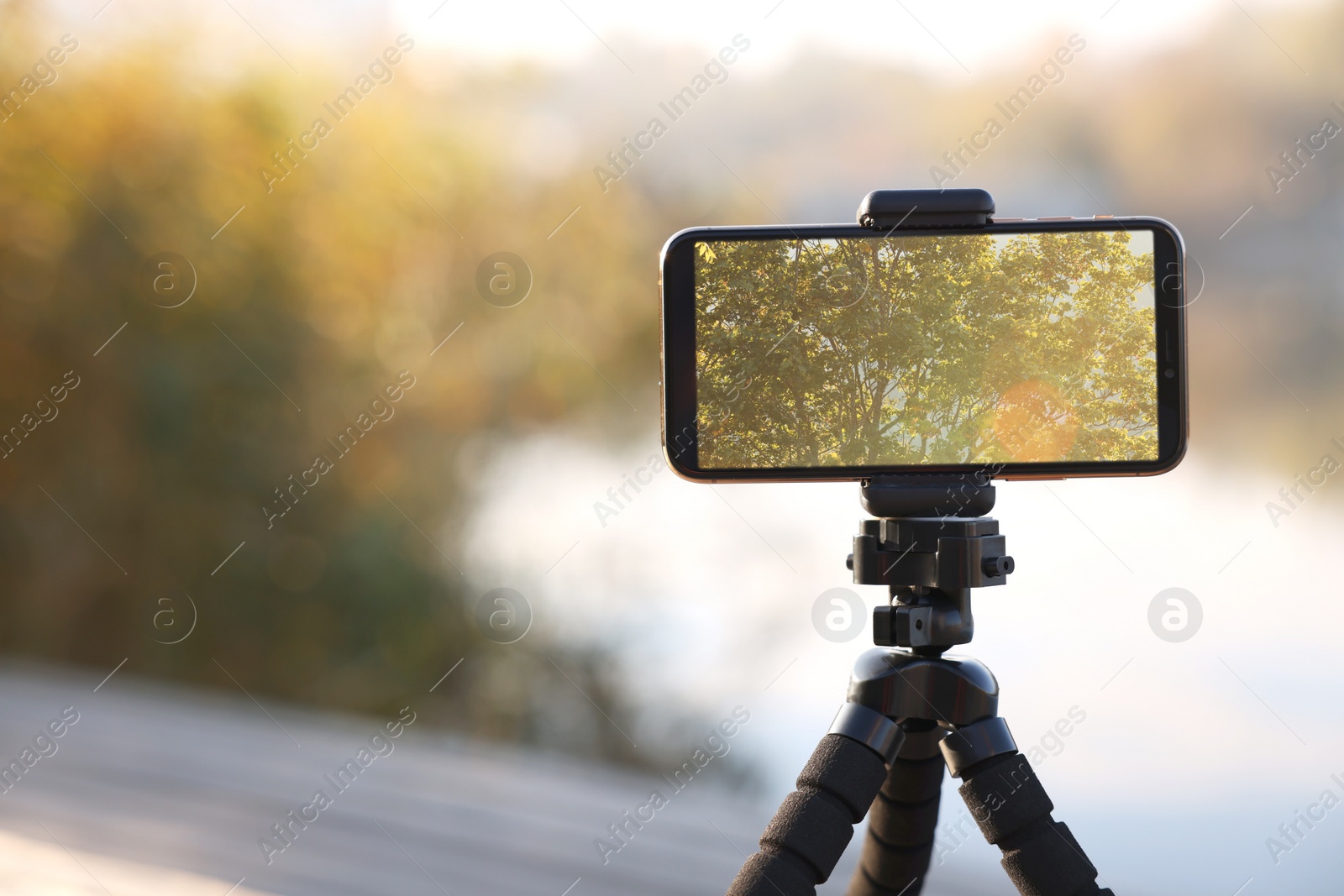 Photo of Tripod with smartphone near river. Space for text