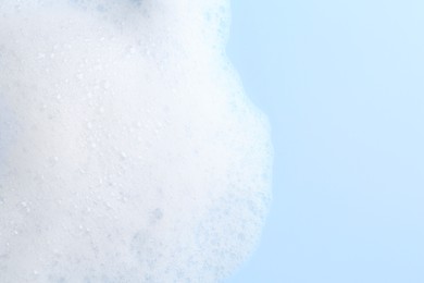 Photo of White fluffy foam on light blue background, top view. Space for text