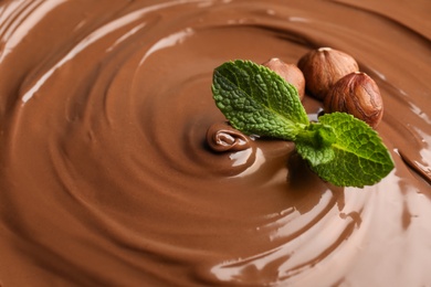 Photo of Sweet tasty chocolate cream with hazelnuts and mint as background, closeup