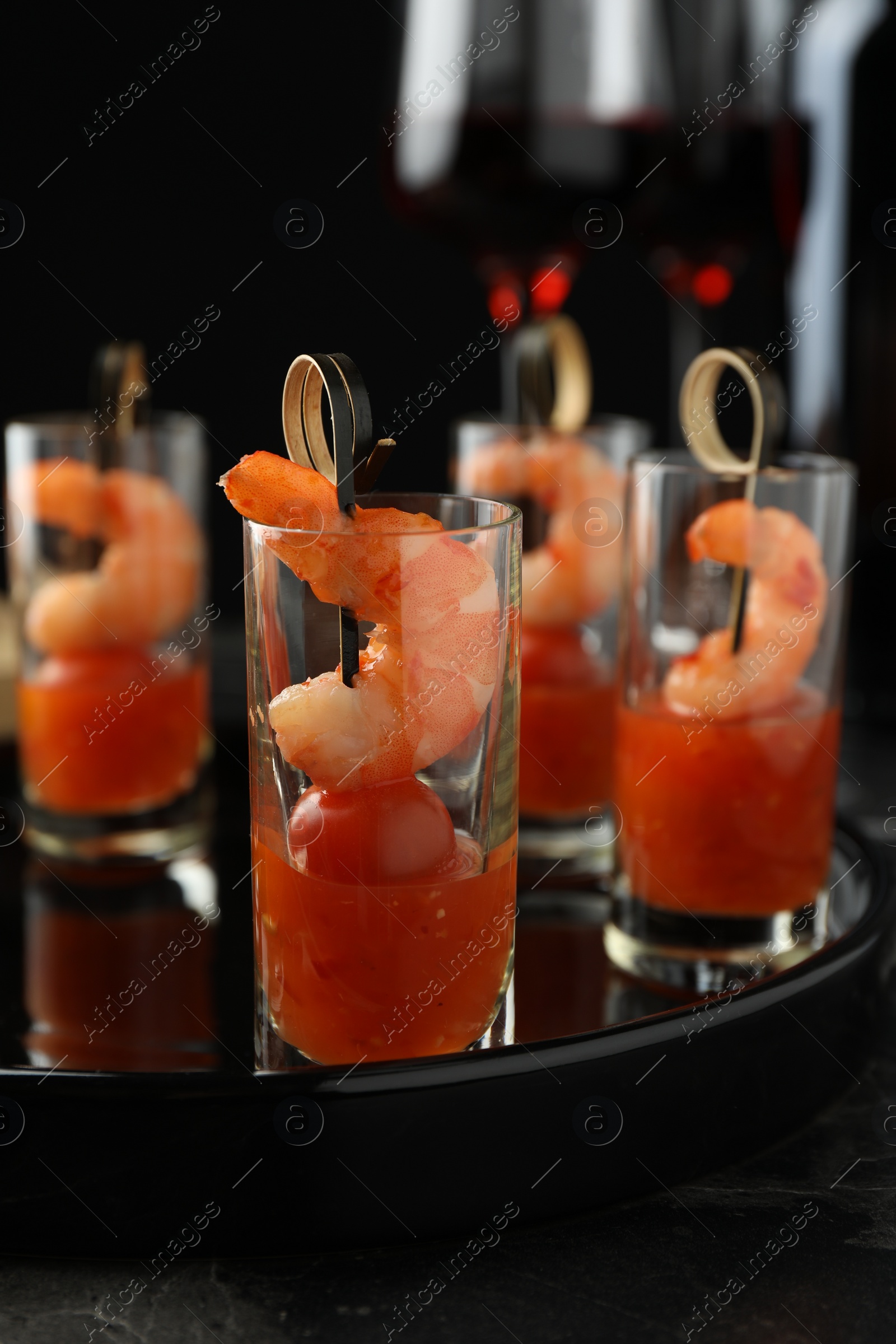 Photo of Tasty canapes with shrimps, tomatoes and sauce in shot glasses on black table, closeup