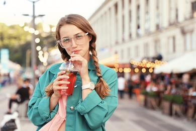 Young woman with refreshing drink on city street. Space for text