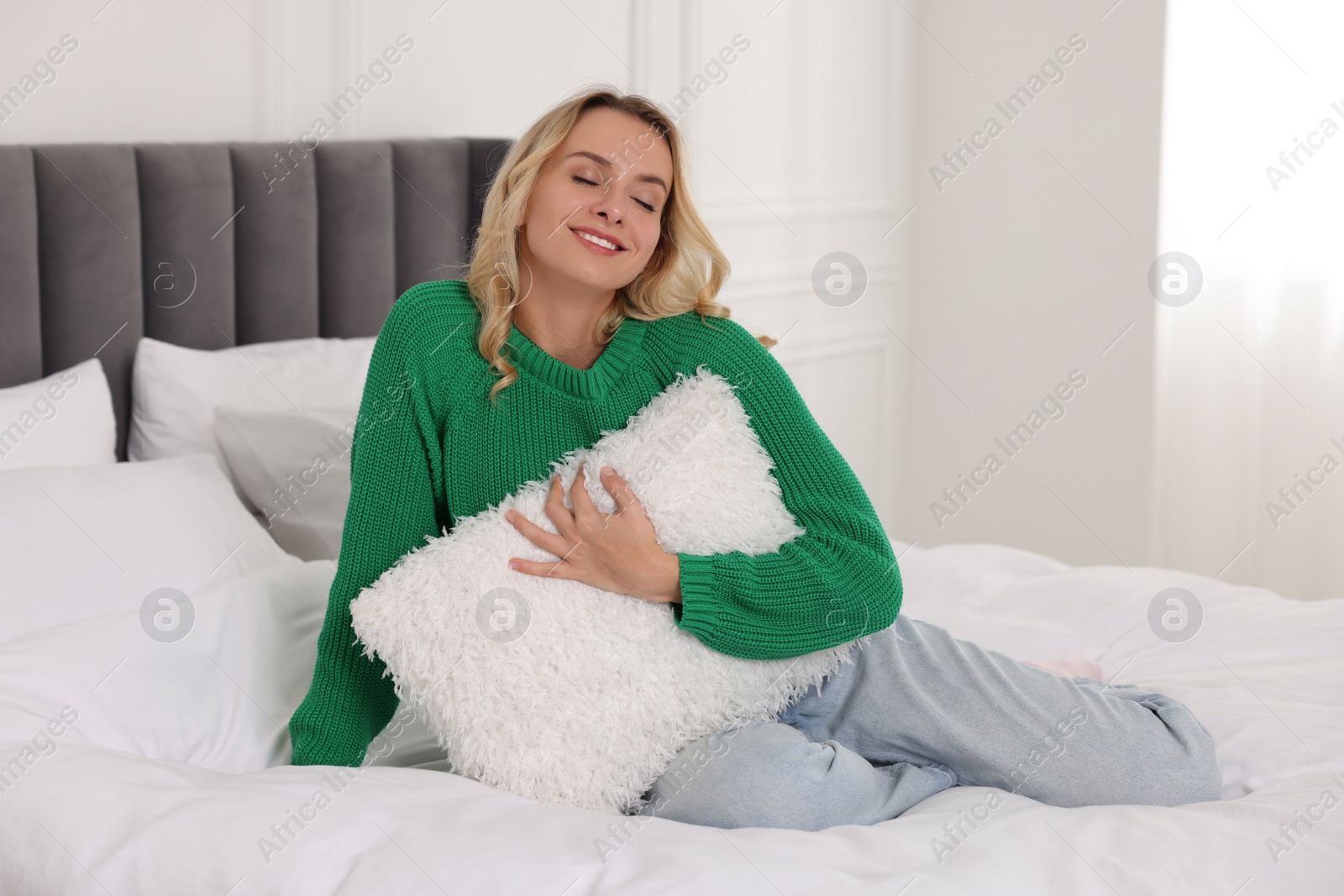 Photo of Happy woman with pillow wearing stylish warm sweater on bed at home