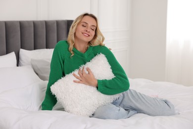 Happy woman with pillow wearing stylish warm sweater on bed at home