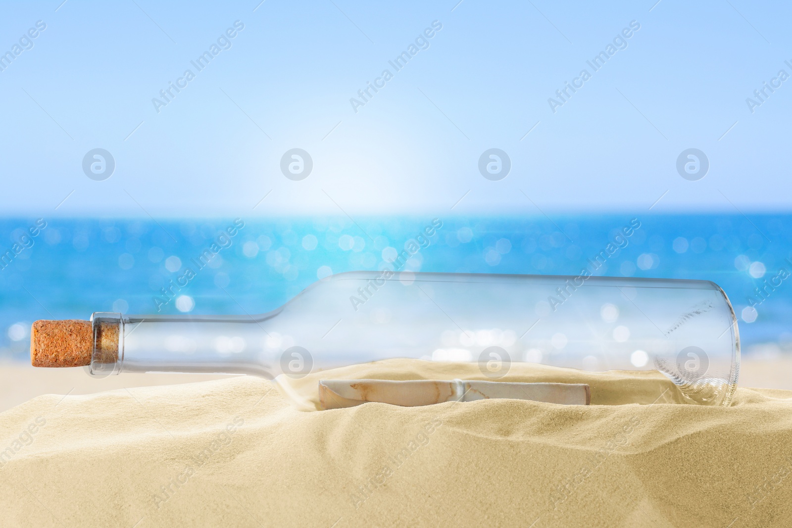 Image of Corked glass bottle with rolled paper note on sandy beach near ocean