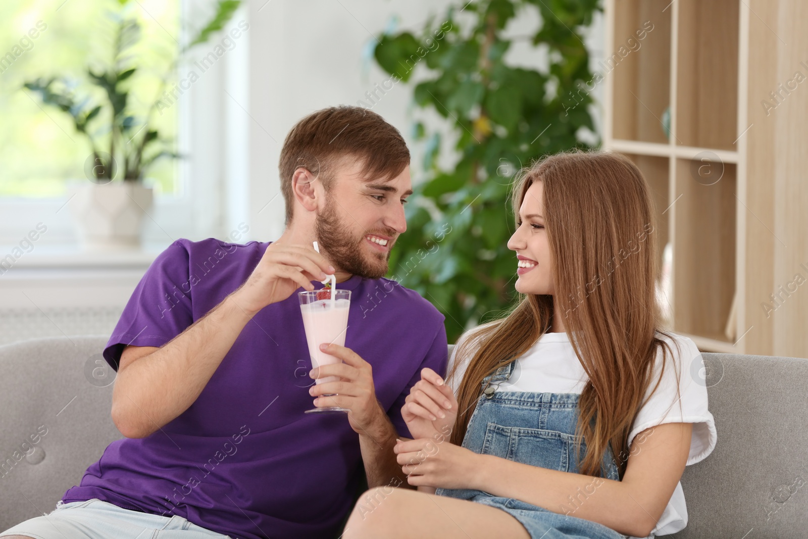 Photo of Young couple with glass of delicious milk shake indoors