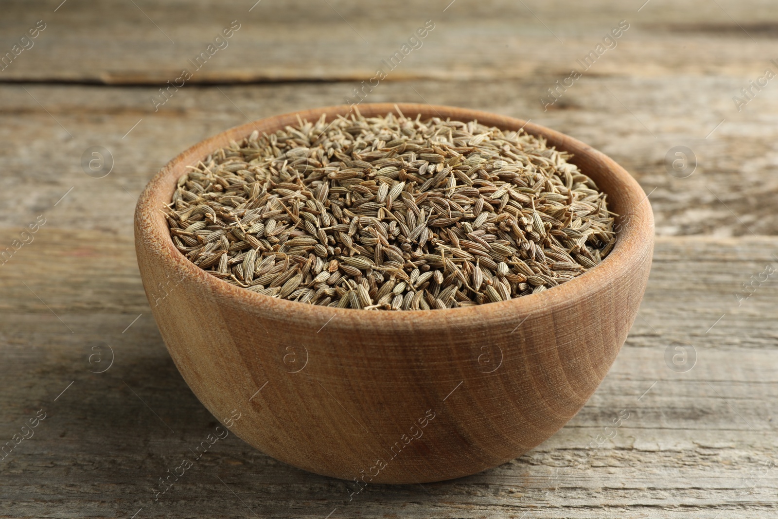 Photo of Bowl of caraway seeds on wooden table, closeup