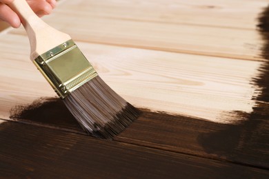 Man with brush applying wood stain onto wooden surface, closeup. Space for text