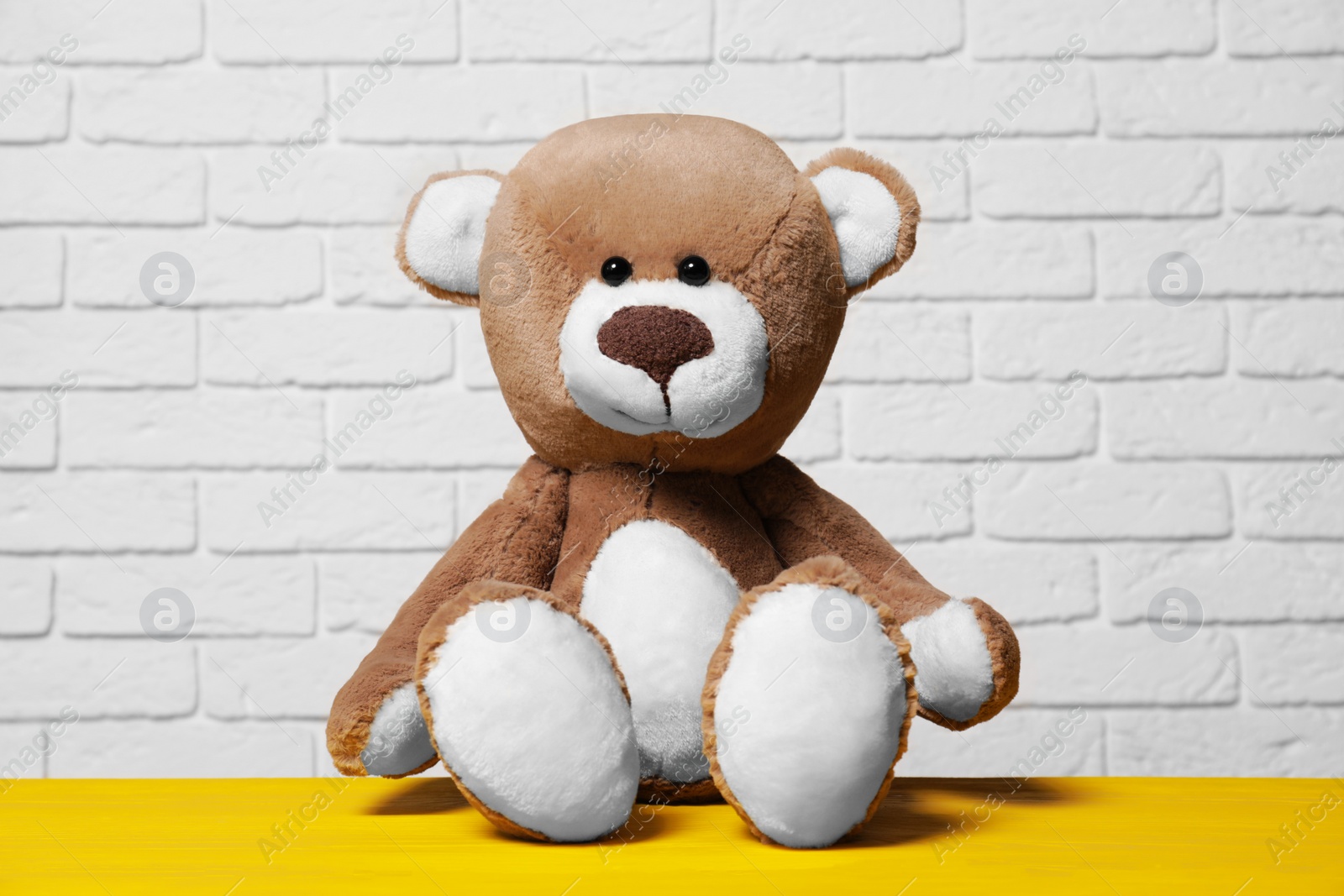 Photo of Cute teddy bear on yellow wooden table near white brick wall