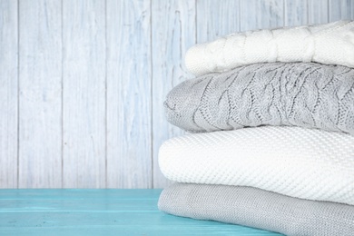 Image of Stack of folded warm sweaters on turquoise wooden table. Space for text