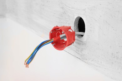 Photo of Hole for socket with wires in wall indoors, closeup. Installation of electrical wiring