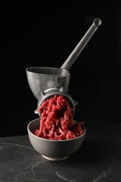 Metal meat grinder with beef mince on dark textured table against black background