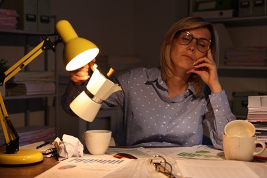 Overwhelmed woman pouring coffee onto documents while snoozing at workplace in office at night