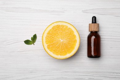 Photo of Bottle of citrus essential oil and fresh orange on white wooden table, flat lay