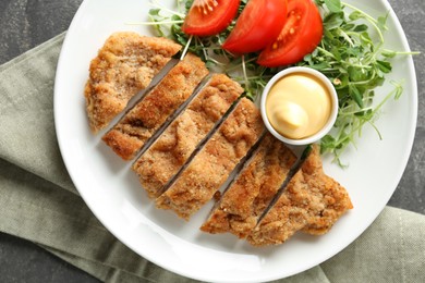 Tasty cut schnitzel served with sauce, microgreens and tomato on grey table, top view
