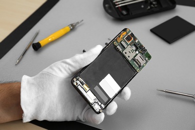 Technician repairing broken smartphone at table, closeup