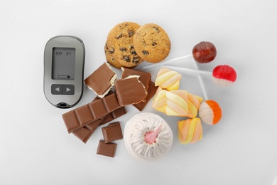 Photo of Digital glucometer and sweets on white background, top view. Diabetes concept
