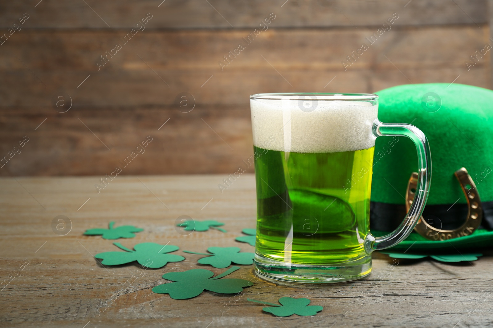 Photo of Green beer, hat and clover leaves on wooden table, space for text. St. Patrick's Day celebration