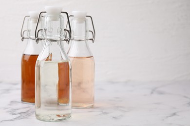 Photo of Different types of vinegar in bottles on light marble table, closeup. Space for text