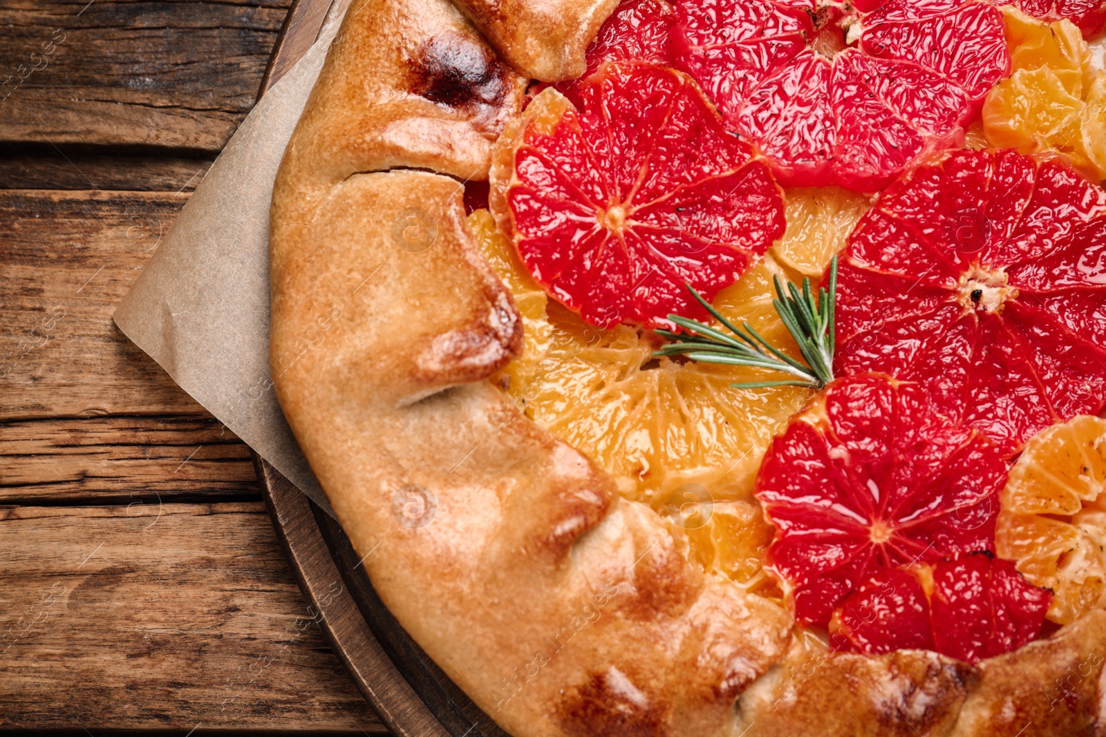 Photo of Tasty galette with citrus fruits and rosemary on wooden table, top view