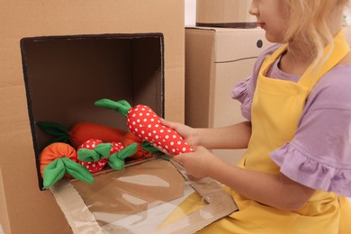 Photo of Little girl playing with toy cardboard oven indoors, closeup