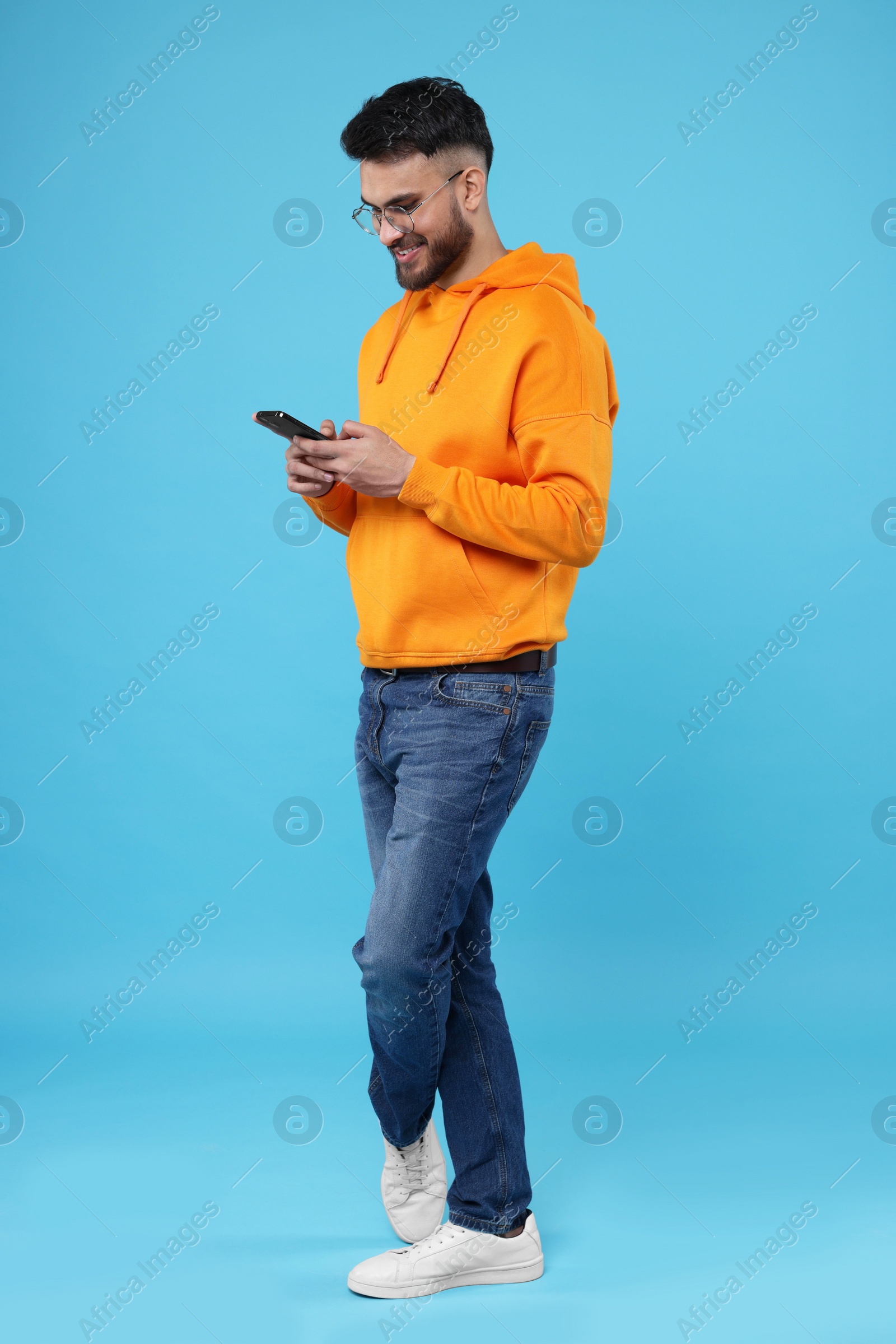 Photo of Happy young man using smartphone on light blue background