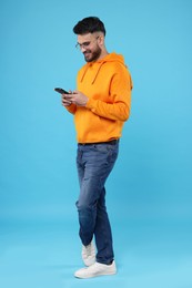 Happy young man using smartphone on light blue background