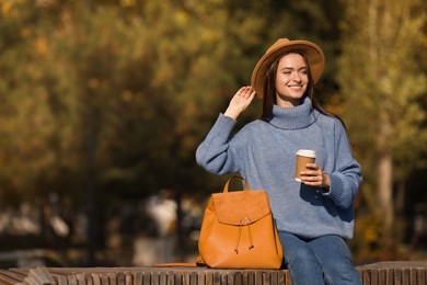 Photo of Young woman with stylish backpack and hot drink on autumn day, space for text