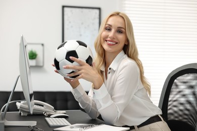 Photo of Happy woman with soccer ball at table in office