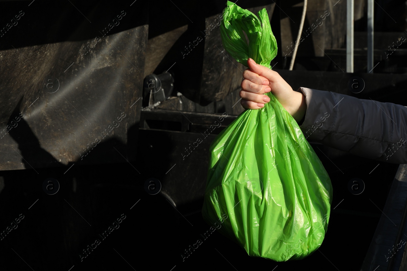 Photo of Woman throwing trash bag full of garbage in bin outdoors, closeup