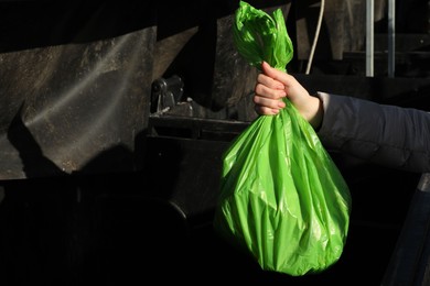 Photo of Woman throwing trash bag full of garbage in bin outdoors, closeup