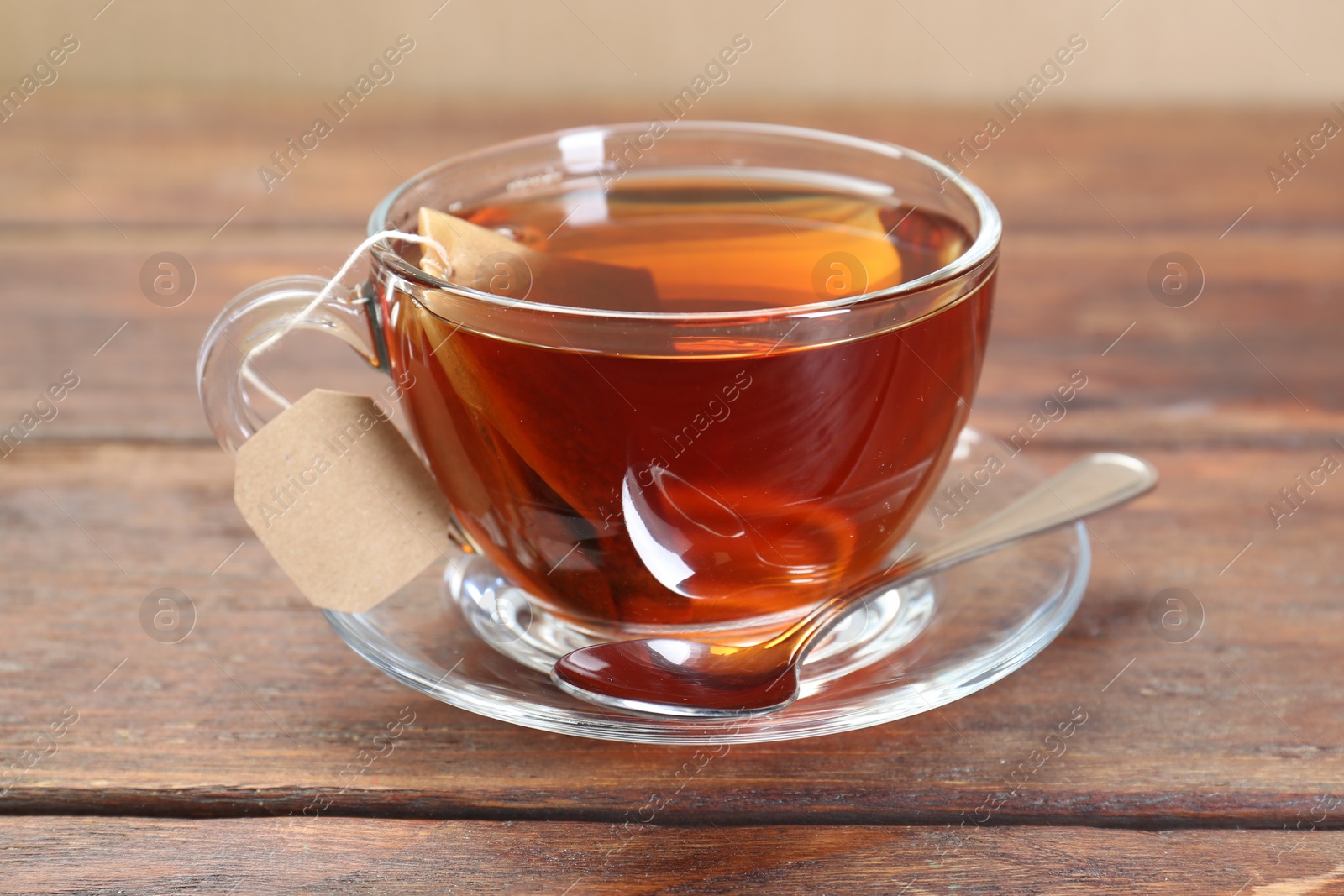 Photo of Brewing aromatic tea. Cup with teabag and spoon on wooden table