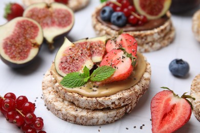 Photo of Tasty crispbreads with peanut butter, figs and berries on light table, closeup